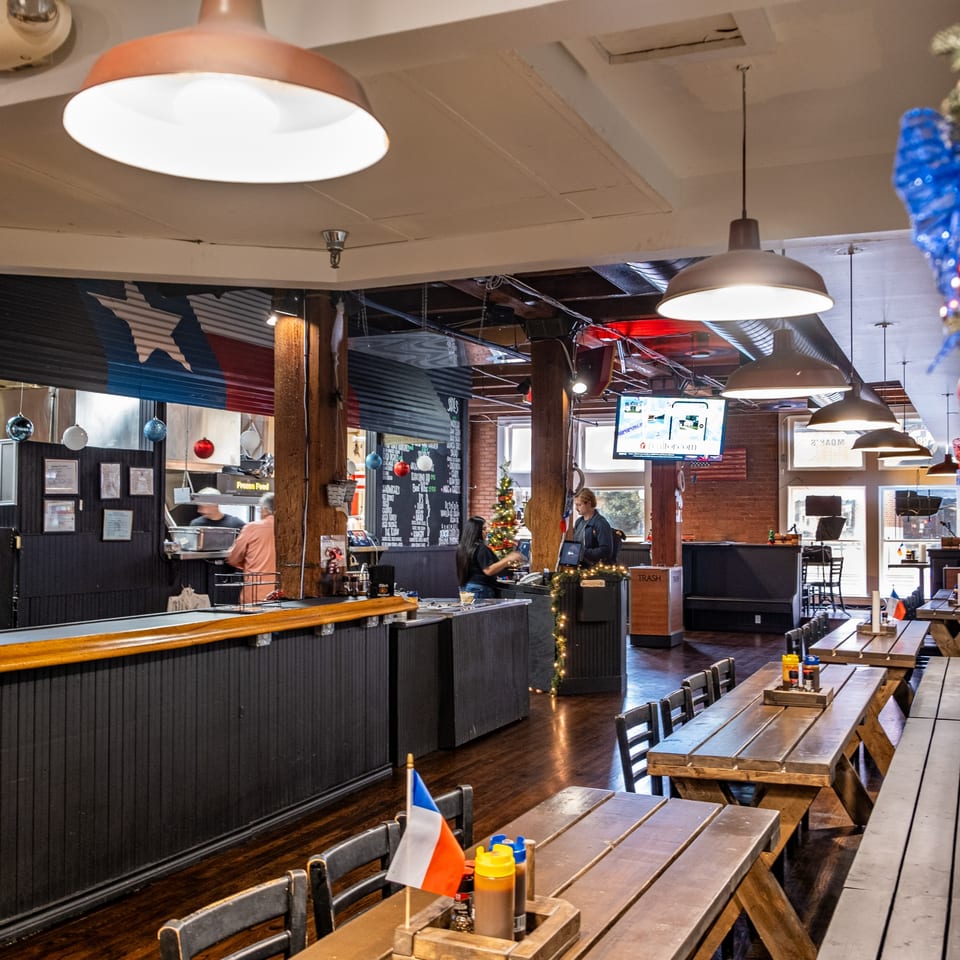 Interior of Moak's Family Texas BBQ, featuring wooden picnic tables, a counter, and a Christmas tree.