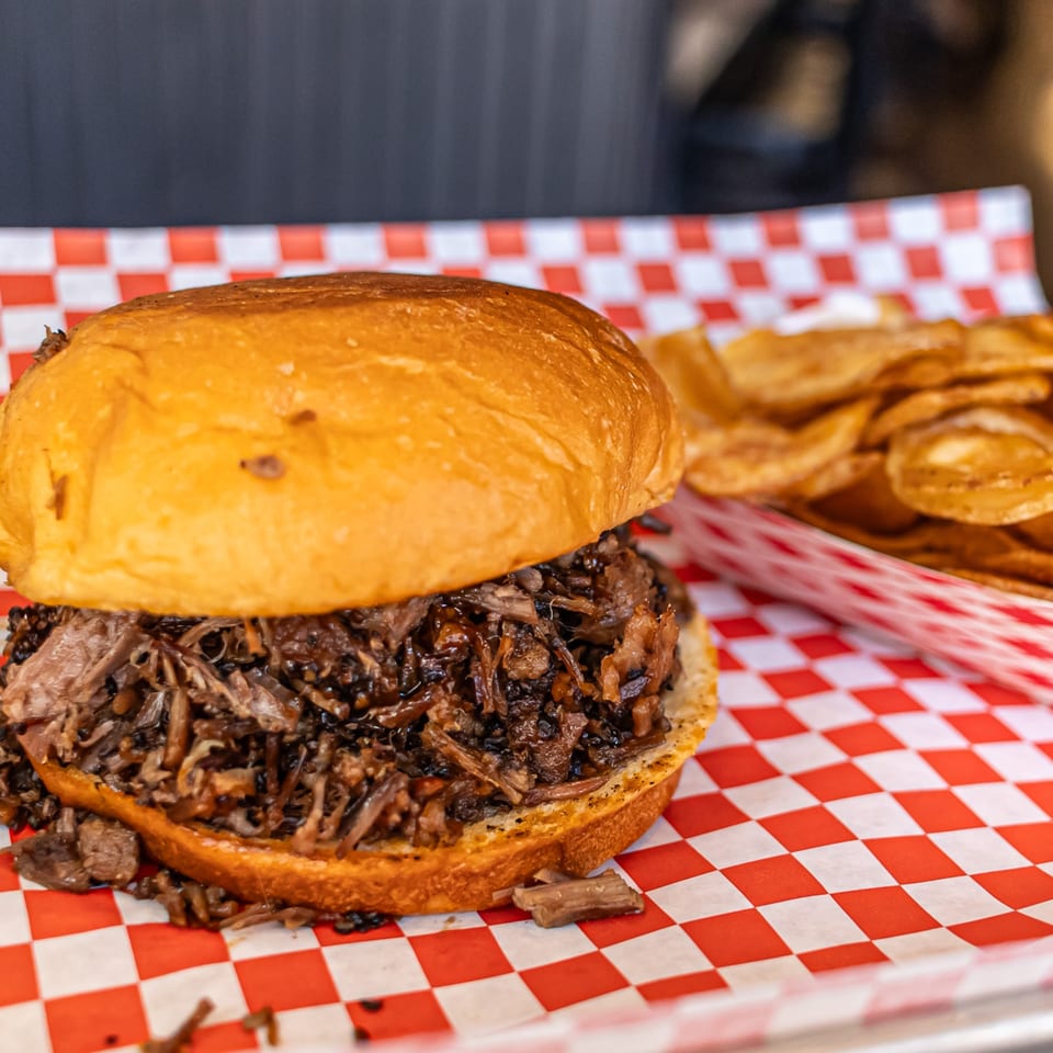 Moak's Family Texas BBQ pulled pork sandwich with chips on red and white checkered paper.