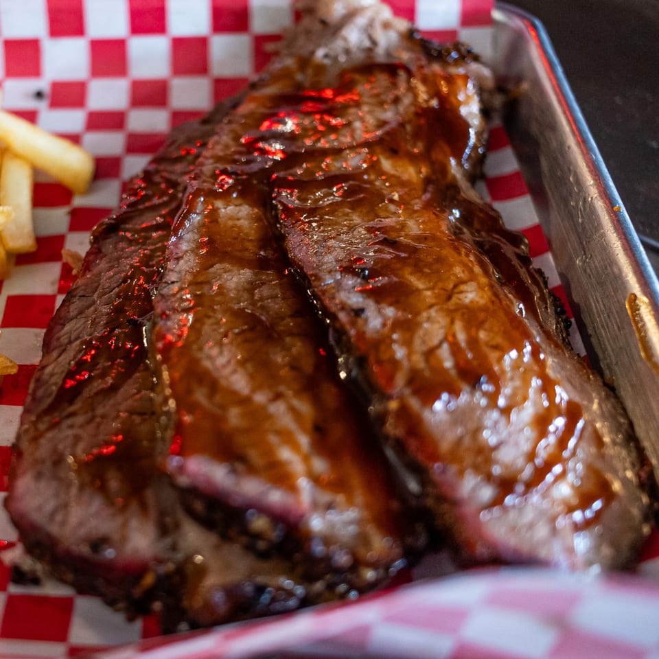 Moak's Family Texas BBQ brisket slices with glistening sauce and a side of fries on checkered paper.