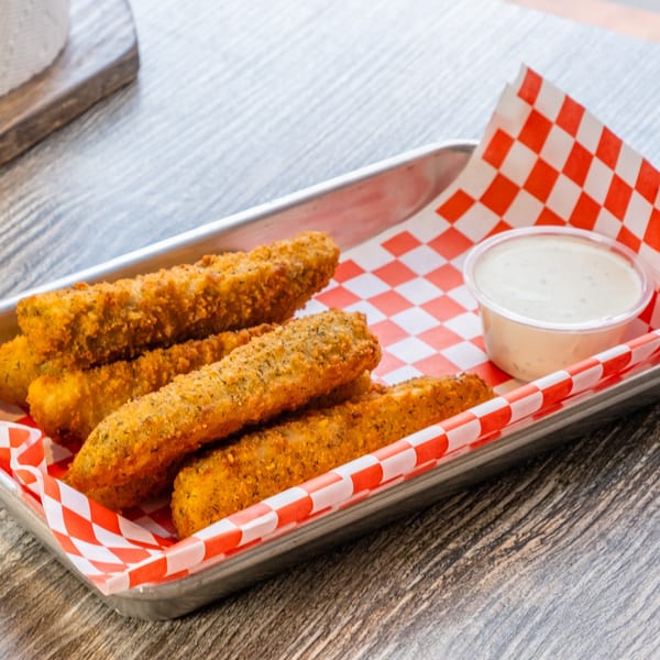 Fried pickle spears with ranch dressing on a metal tray with red and white checkered paper.