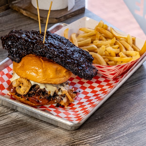 A Moak's Family Texas BBQ burger with a large rib on top, onion rings, and fries.