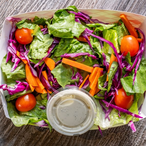 Fresh side salad with green lettuce, red cabbage, carrots, cherry tomatoes, and ranch dressing.