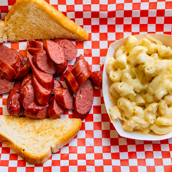 Sliced Moak's Family Texas BBQ sausage, mac and cheese, and Texas toast on red checkered paper.
