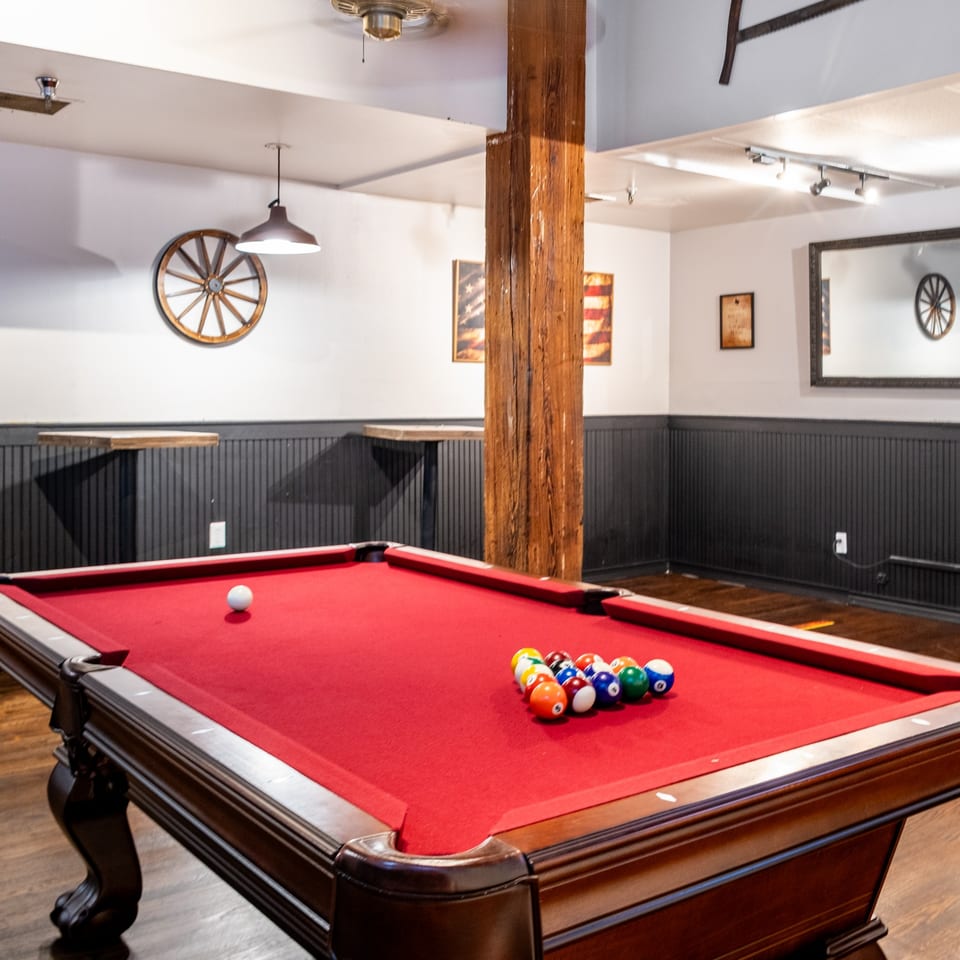 Red felt pool table with racked balls and cue ball in a rustic game room.
